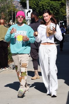 a man and woman walking down the street with coffee in their hands while wearing sweatpants