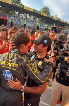 two men hug each other in front of a crowd at a race track with cameras around them