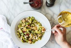 a white bowl filled with green vegetables next to a glass of wine on a marble table