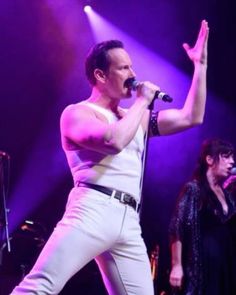 a man standing on stage with his hands up in the air while singing into a microphone