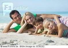 a family laying on the beach with their arms around each other and smiling at the camera