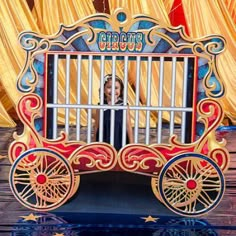 an elaborately painted cart with wheels on display at a carnival or fair, in front of curtained yellow drapes