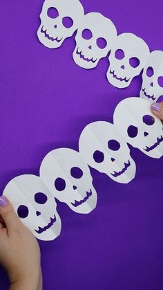 someone is cutting out paper skulls on a purple background