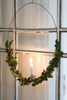 a candle is lit in the middle of a wreath hanging on a window sill