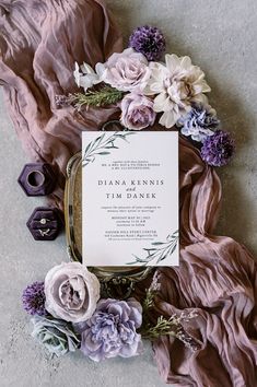 the wedding stationery is surrounded by purple flowers and greenery