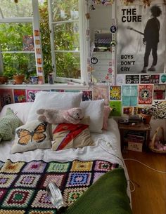 a bed with lots of pillows and blankets on it in a room filled with posters