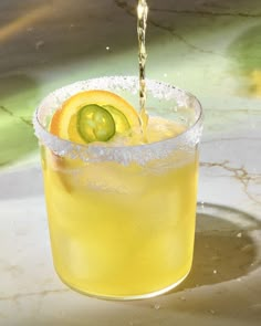 a drink being poured into a glass with cucumber on the rim and ice