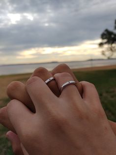 two hands holding each other in front of the ocean and cloudy sky with trees behind them