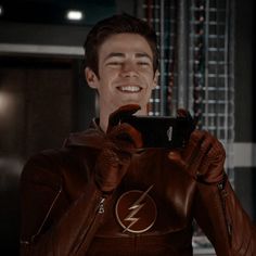 a man in a leather jacket holding up a cell phone to his face with the flash logo on it