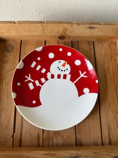 a red and white plate with a snowman painted on the front sitting on a wooden table