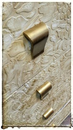 two brass handles on an ornate white cabinet with intricate embosishments and floral designs