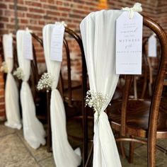 the chairs are lined up with white flowers and ribbons tied to them, along with place cards