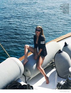 a woman is sitting on the back of a boat in front of water and wearing sunglasses