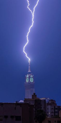 a clock tower with lightning striking in the sky