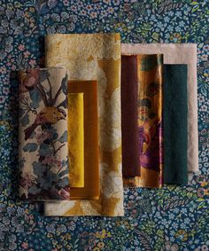 four different colored fabrics hanging on a wall with floral designs and flowers in the background