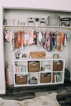 an organized closet with baskets and clothes hanging on the wall next to shelves filled with baby's clothing