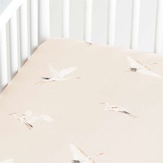 a crib sheet with white birds flying in the sky on it's side