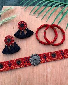 red and black beaded jewelry sitting on top of a wooden table next to a plant