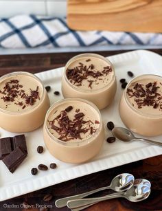 four desserts are sitting on a plate with spoons and chocolate chips next to them