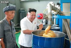 two men standing in front of a blue pot filled with yellow donuts and smiling