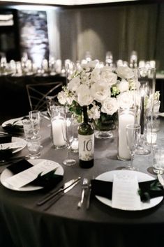 the table is set with white flowers, candles and place settings for an elegant dinner