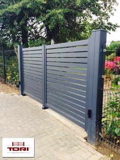 a blue gate is on the side of a brick walkway next to a flower garden