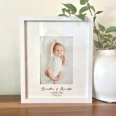 a white frame holds a baby's photo and is next to a potted plant