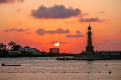 the sun is setting behind a lighthouse on the water