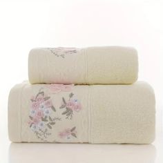 two white towels with pink flowers on them are stacked next to each other in front of a white background