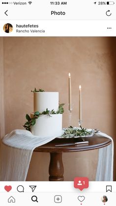 a white cake sitting on top of a wooden table next to two candles and greenery