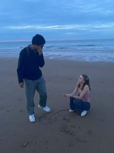 a man and woman on the beach with footprints in the sand while talking on their cell phones