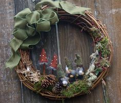 a wreath with gnomes and pine cones is hung on a wooden fence, next to a green bow