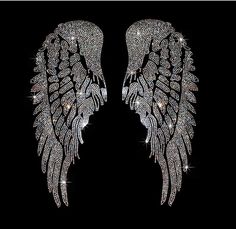 two large white wings with sparkling crystals on them, against a black background in the shape of an angel's wings