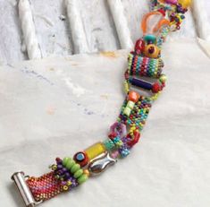 a multi - colored beaded bracelet is displayed on a white surface with an object in the background