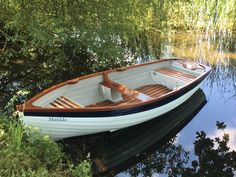 there is a small boat that is docked in the water by some grass and trees