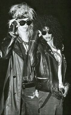 two people in leather jackets and sunglasses standing next to each other with their hands on their faces