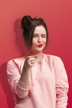 a woman in pink sweater holding her hand up to her face and looking at the camera