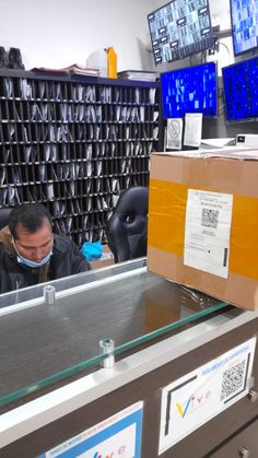 a man wearing a face mask sitting at a desk in an office with boxes on it