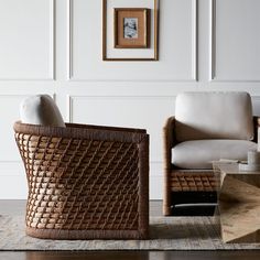 two wicker chairs sitting next to each other in front of a white wall with framed pictures on it