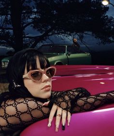 a woman with black hair and sunglasses leaning on a pink surfboard