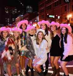 a group of women in pink hats pose for a photo on the street at night