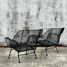 two black chairs sitting next to each other on the ground in front of a wall