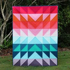 a colorful quilt on the grass with trees in the backgroung behind it