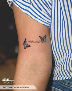 a woman's arm with two butterflies on it and the date tattoo by vidii nevada