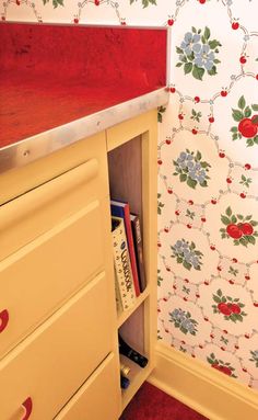 an old dresser with red drawers and floral wallpaper