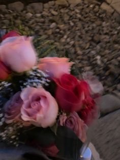 a vase filled with pink and red flowers on top of a wooden table next to rocks