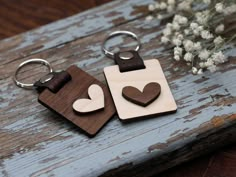 two wooden keychains with hearts on them sitting on a table next to flowers