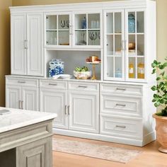 a kitchen with white cabinets and marble counter tops in front of a potted plant