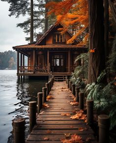 a wooden dock leading to a small house on the water with fall leaves around it