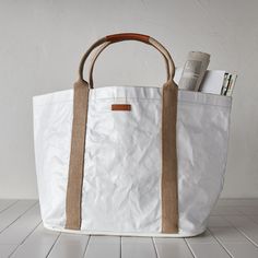 a white tote bag with brown straps and books on the bottom, sitting on a tile floor